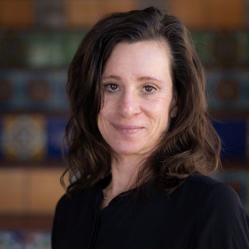 Professional headshot of a woman with shoulder-length brown hair in a black blouse, smiling at the camera.